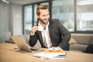 man holding white teacup in front of gray laptop