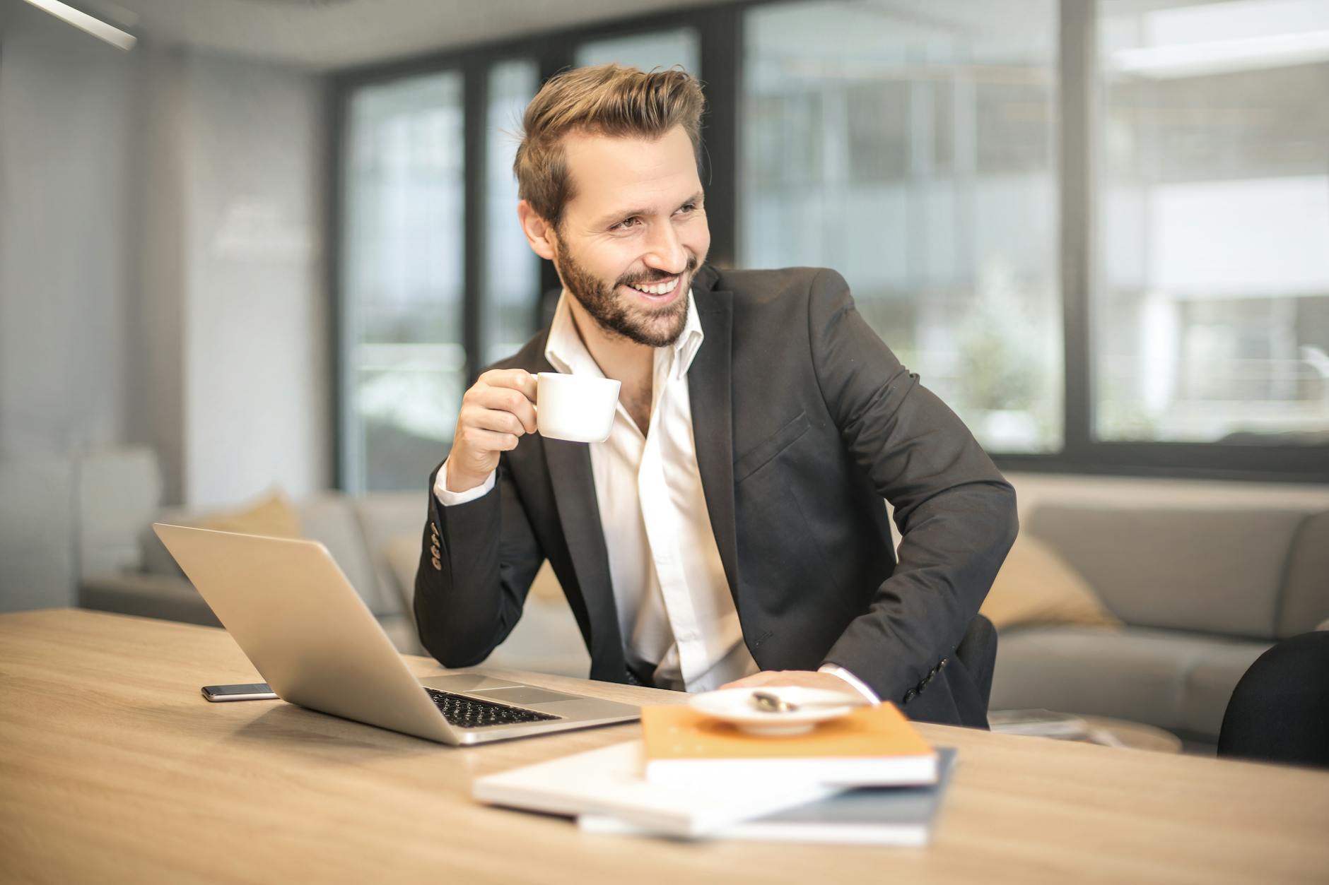 man holding white teacup in front of gray laptop